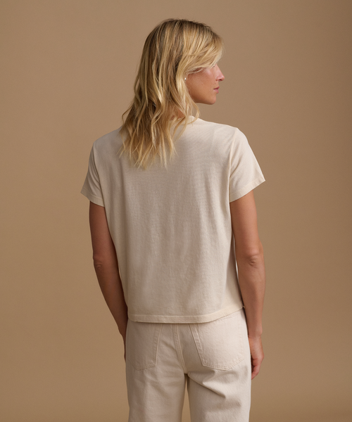 A model wearing a cream t-shirt with cream jeans against a beige studio background.