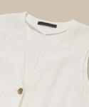 A close-up of the Callan Dress, a sleeveless white linen staple with a V-neckline and single brown button, displayed flat on a beige background with a black label inside the collar.