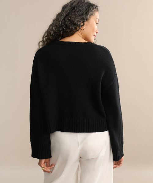 A person with long, wavy hair is shown from the back wearing the Cameron Crewneck in black and light-colored pants, standing against a neutral beige background.