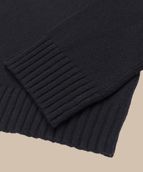 Close-up of the sleeve and hem of the Cameron Crewneck, a black knit sweater with ribbed cuffs, shown on a neutral beige background.