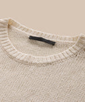 Close-up of the Cameron Crewneck, a cream-colored sweater with a ribbed neckline and black label inside the collar, shown against a beige background—a lightweight piece ideal for layering.