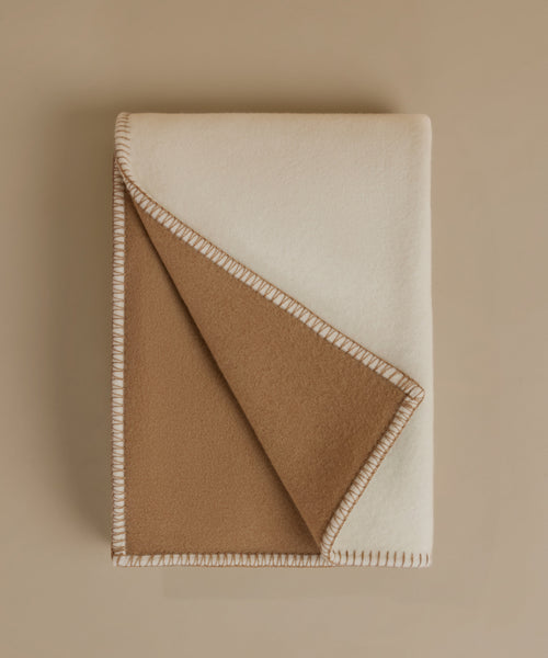 A cream-colored blanket with a stitched border, photographed flat on a matching beige background.