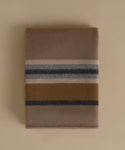 A folded wool blanket with a classic stripe pattern in taupe, camel, navy, and cream, displayed on a solid beige background.