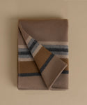 A folded wool blanket with a classic stripe pattern in taupe, camel, navy, and cream, displayed on a solid beige background.