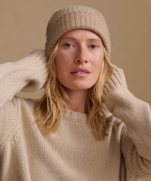 Woman wearing an oatmeal color cashmere sweater with a matching ribbed beanie.