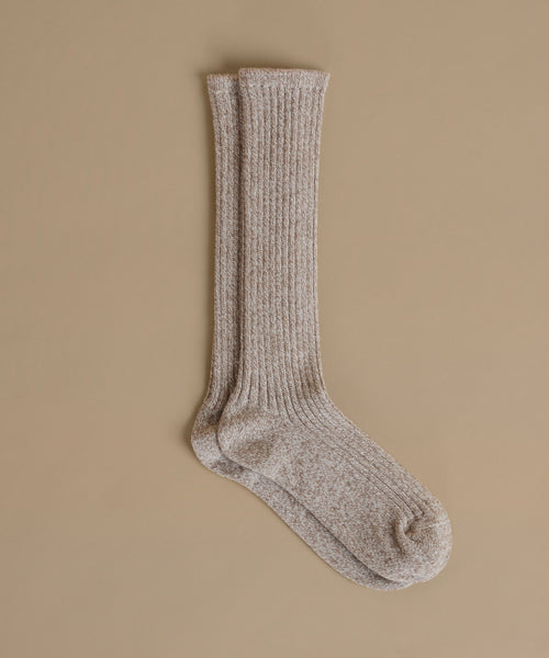 A pair of ribbed knit crew socks in a heathered taupe-beige color, displayed against a solid beige background.