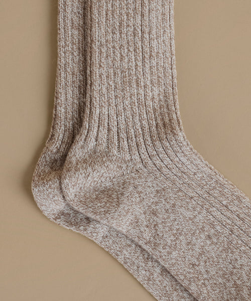 A close-up of a pair of ribbed knit socks in a heathered taupe-brown and cream colorway, displayed against a solid beige background.