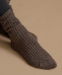 A close-up of a ribbed knit sock worn on a foot, shown against a plain warm beige background.