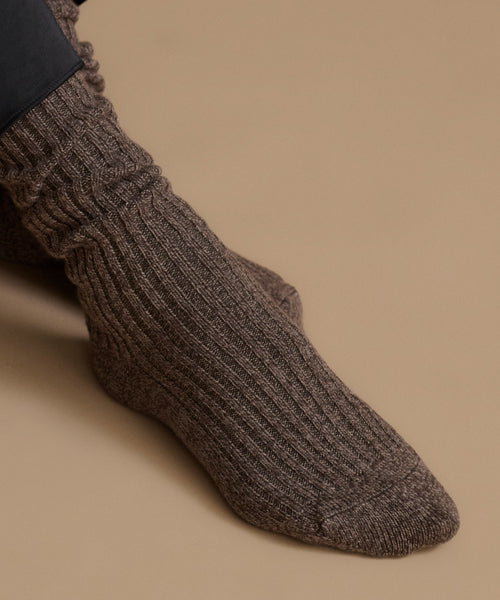 A close-up of a ribbed knit sock worn on a foot, shown against a plain warm beige background.