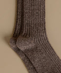A close-up of a ribbed knit sock in a heathered brown and beige colorway, displayed against a solid beige background.