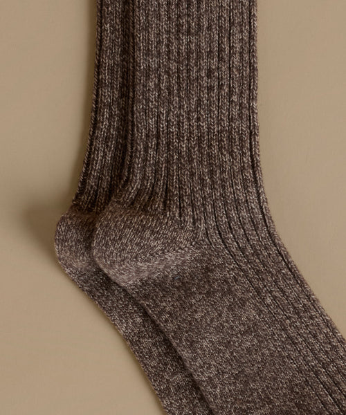 A close-up of a ribbed knit sock in a heathered brown and beige colorway, displayed against a solid beige background.