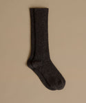 A single dark charcoal gray ribbed knit sock displayed against a solid beige background.