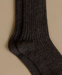 A close-up of a pair of dark charcoal gray ribbed knit socks on a solid beige background.