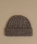 A dark brown and black marled knit beanie hat with a ribbed cuff, displayed flat against a solid beige background.