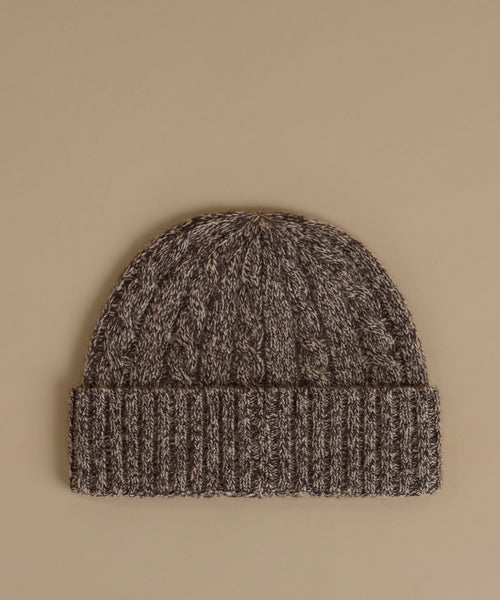 A dark brown and black marled knit beanie hat with a ribbed cuff, displayed flat against a solid beige background.