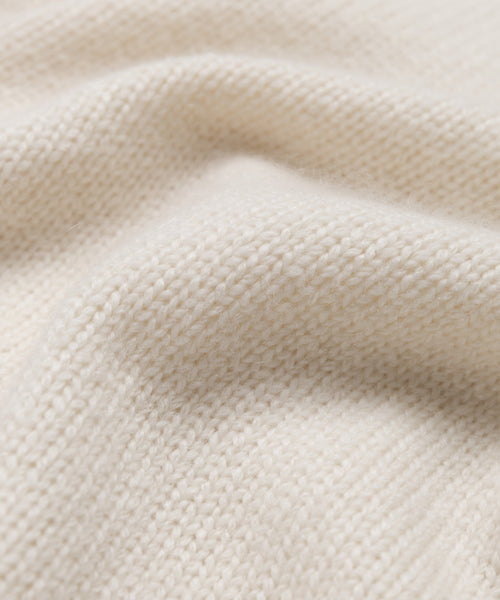 Close-up of the Cashmere Kate V-Neck features soft, cream-colored cashmere knit fabric with a visible textured pattern and gentle folds, highlighting its cozy and warm feel.