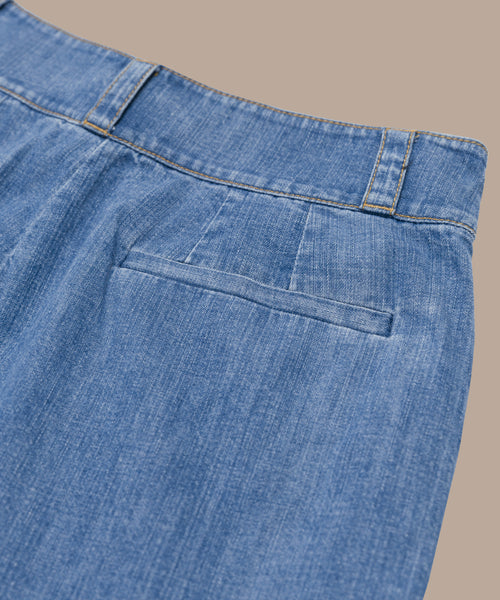 Close-up of the back of the blue Denim Newport Trouser with a single back pocket and visible stitching, ideal for spring and summer. Shown against a beige background. Pair with the Parker Oversized Shirt for effortless style.