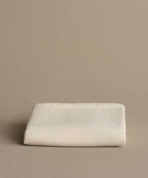 The Chateau Alpaca Coverlet, soft and neatly folded with stitched edges, rests on a plain beige surface against a matching beige background.