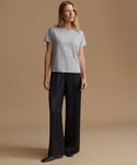 A woman modeling a light gray short-sleeve crewneck t-shirt and black wide-leg trousers against a solid beige studio background.