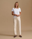 A woman modeling a white short-sleeve crewneck t-shirt and cream wide-leg trousers, paired with dark brown loafers, against a solid beige studio background.