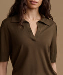 A close-up of a woman wearing a short-sleeve knit polo shirt in olive brown against a solid beige background.
