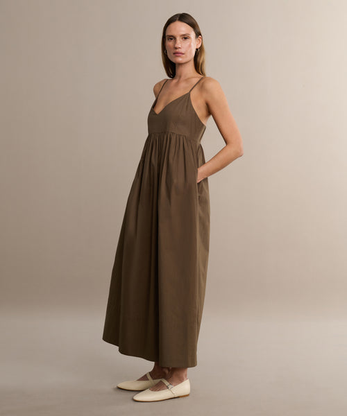 Wearing the Cove Dress, a woman exudes casual flair in its brown cotton fabric and relaxed fit—perfect for any easygoing day.