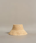 The Crochet Raffia Sun Hat, in a natural hue with a wide brim and simple woven texture, is displayed on a plain light gray background.