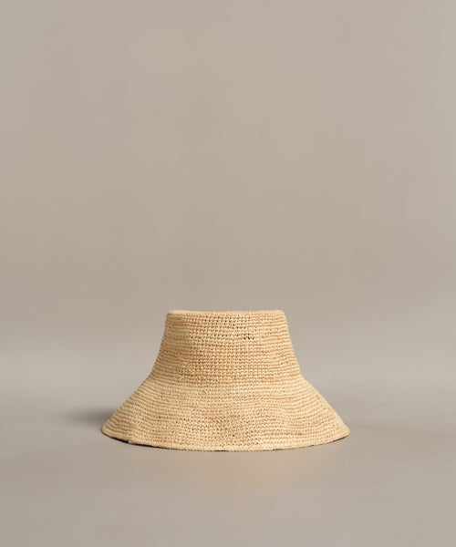 The Crochet Raffia Sun Hat, in a natural hue with a wide brim and simple woven texture, is displayed on a plain light gray background.