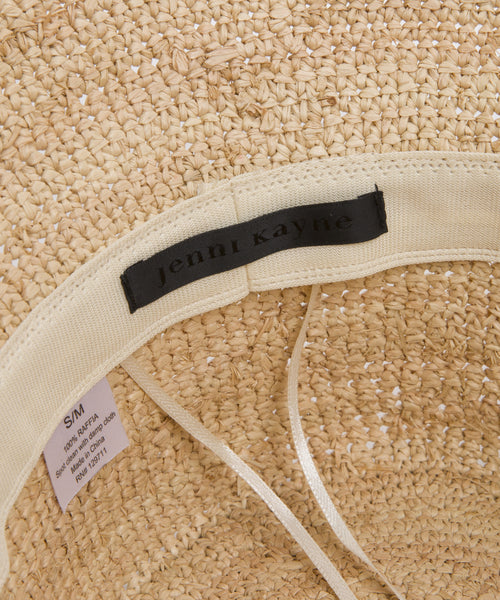 Close-up of the inside of the Crochet Raffia Sun Hat, highlighting a fabric label with jenni kayne stitched on it, plus a size tag marked S/M and visible care instructions.