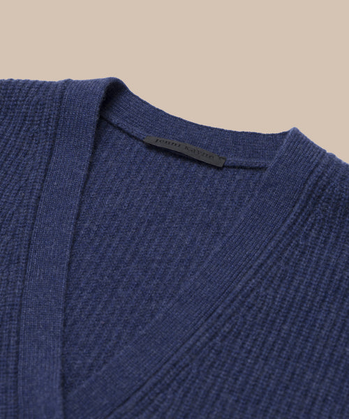 Close-up of the Cropped Cashmere Cocoon Cardigan in navy blue with a ribbed knit and V-neckline, displayed against a beige background. The inside collar shows an unreadable clothing label.