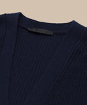 Close-up of the Cropped Cashmere Cocoon Cardigan in navy, featuring a ribbed knit texture, V-neckline, and a black fabric tag inside the collar, displayed against a neutral beige background.