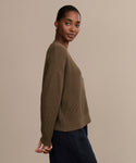 A woman with dark hair pulled back wears the Cropped Cotton Cocoon Cardigan in textured brown with dark pants, standing sideways against a plain beige background and looking at the camera.