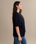 A woman with long brown hair stands in profile against a beige background, wearing the Crosby Tee and classic blue jeans.