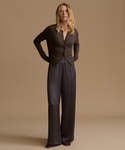 A woman modeling a dark brown long-sleeve cardigan, paired with dark charcoal wide-leg trousers, against a solid beige studio background.
