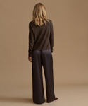 A woman shown from the back wearing a dark brown long-sleeve knit top and matching dark brown wide-leg trousers, standing against a solid beige studio background.