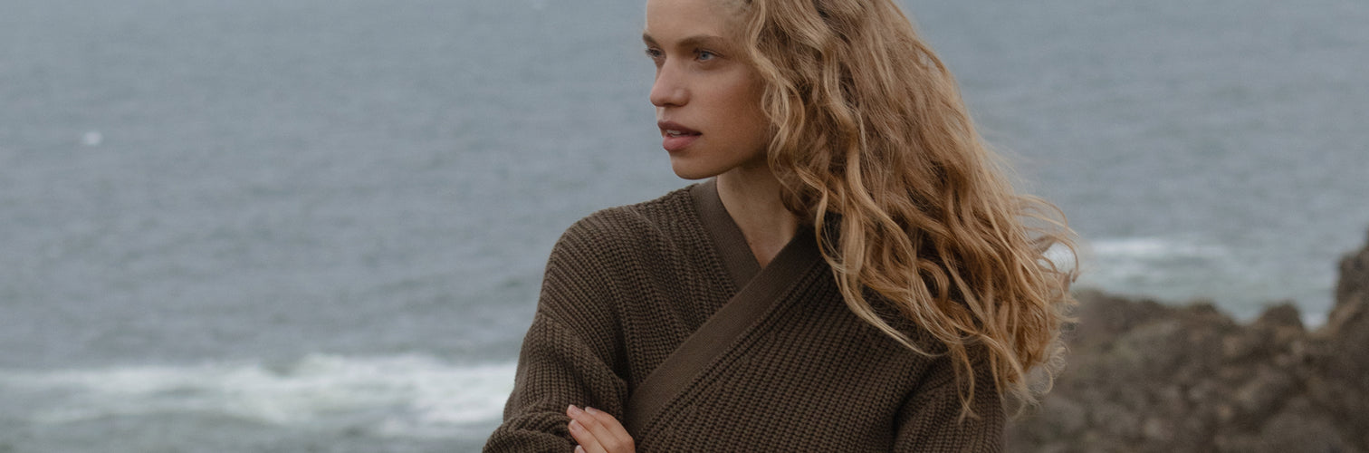 Woman with long blonde hair standing on a beach with ocean waves in the background