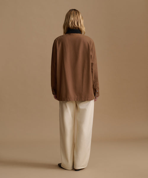 A model viewed from the back wearing a brown jacket and cream wide-leg trousers, set against a solid beige studio background.