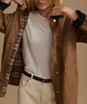 A model wearing a tan jacket over a cream t-shirt and beige trousers, with a plaid lining visible inside the jacket