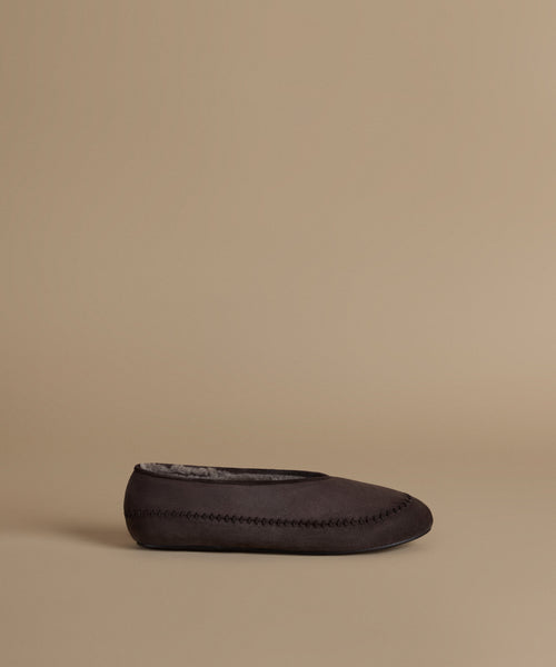 A single dark brown suede slip-on moccasin-style shoe with decorative stitching and a gray plush lining, shown in profile against a solid beige background.