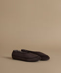 A pair of dark brown suede slip-on slippers with contrast stitching and a soft gray lining, displayed on a solid beige background.