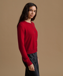A woman wearing a bright red button-front cardigan sweater and black satin trousers, standing against a solid tan studio background.
