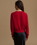 A woman shown from the back wearing a bright red knit sweater and a black skirt, standing against a plain beige studio background.