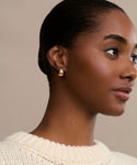 A woman with smooth dark skin and pulled-back hair wears a cream knit sweater and the Felix Dome Hoops, highlighting the elegant gold earrings as she looks right against a neutral backdrop.
