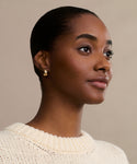 A woman with smooth brown skin and short dark hair pulled back, wearing a cream knit sweater and Felix Dome Hoops, gazes slightly to the side against a neutral background.