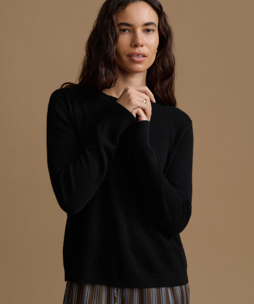 A woman modeling a black long-sleeve knit sweater against a solid warm beige studio background.