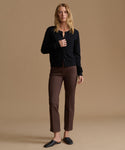 A woman modeling a black button-up cardigan and brown cropped trousers with black mule flats, set against a solid beige studio background.