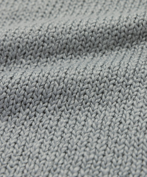 Close-up of the Foster Cotton Sweater, crafted from soft organic Tanguis cotton in light gray, featuring a textured ribbed knit and wavy folds.