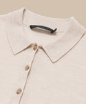 A close-up of the Grayson Pullover, a beige casual polo with a button-down front featuring three visible buttons and an inner black label, laid flat on a matching beige background.