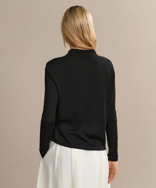 A person with blonde hair is shown from the back, wearing the Grayson Pullover in black and a white skirt, standing against a plain beige background.