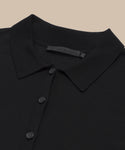 Close-up of the black Grayson Pullover, a casual polo sweater with a button-down front (three visible buttons) and an inner collar fabric tag, laid flat on a beige background.